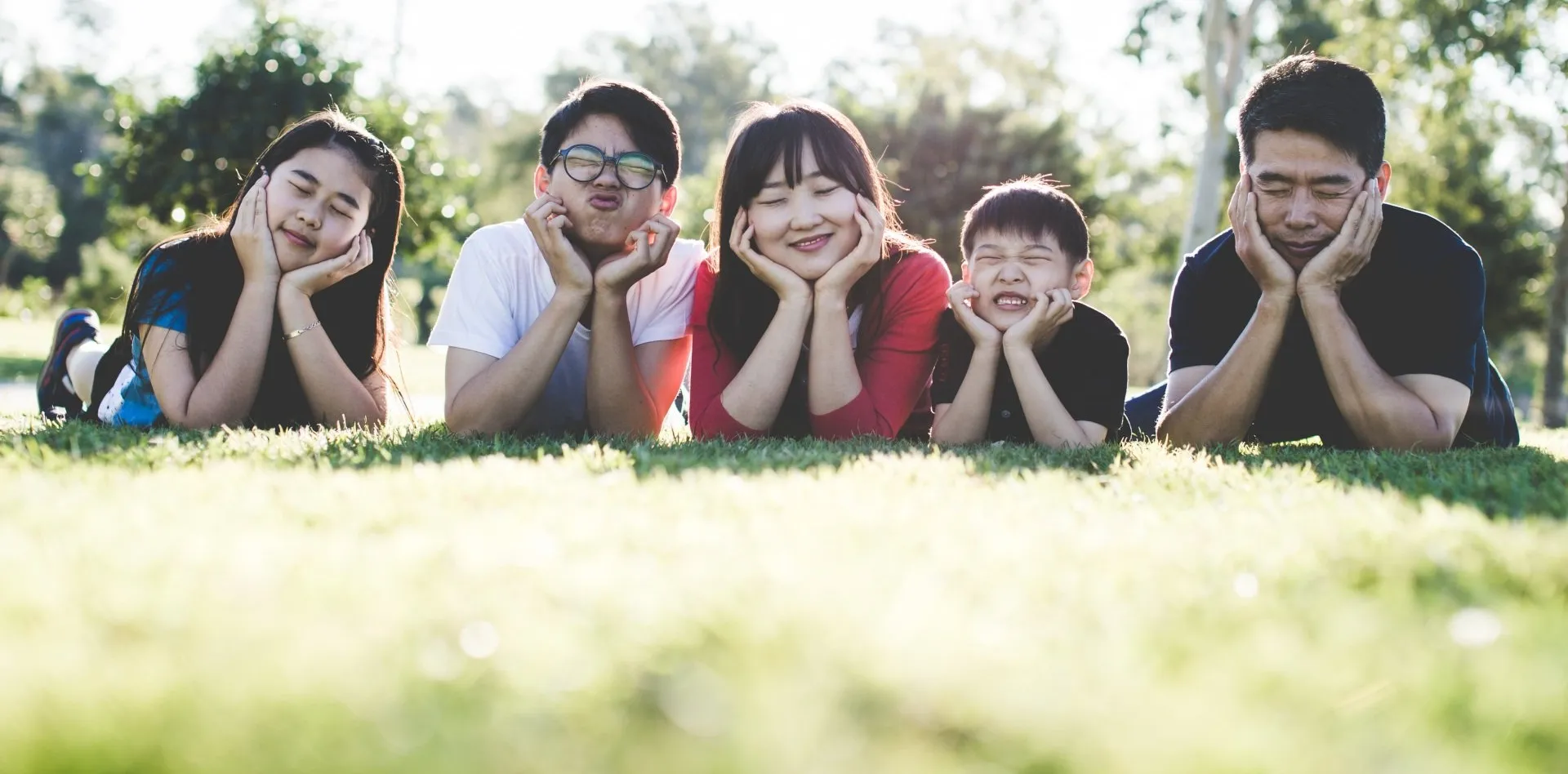 A family laying in the grass with their hands on their face.