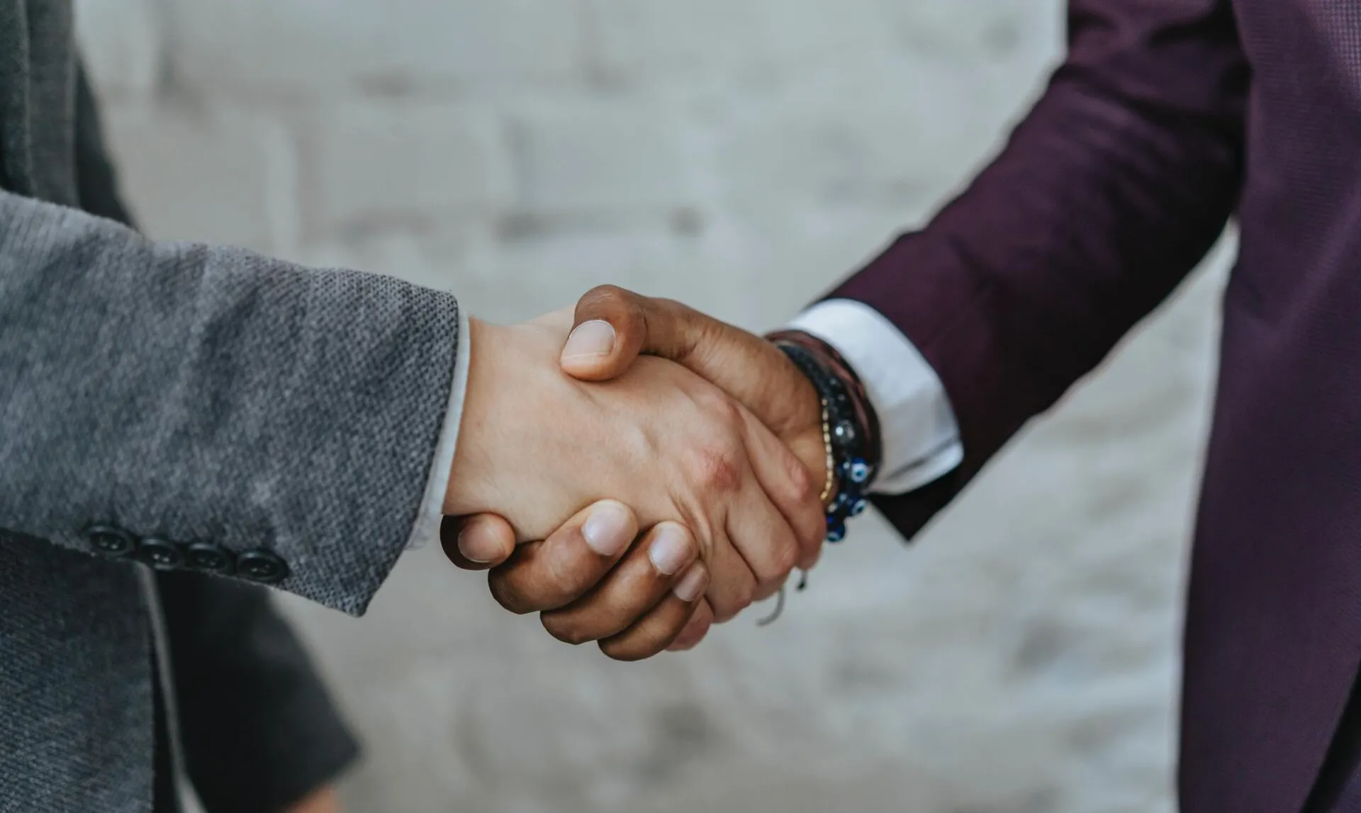 Two people shaking hands in front of a brick wall.